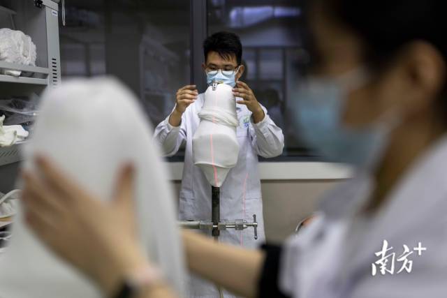 华南辅具中心内，假肢技师钟正科在进行大腿假肢接受腔抽真空成型工作，利用红外水平仪测量假肢模具厂的具体位置。